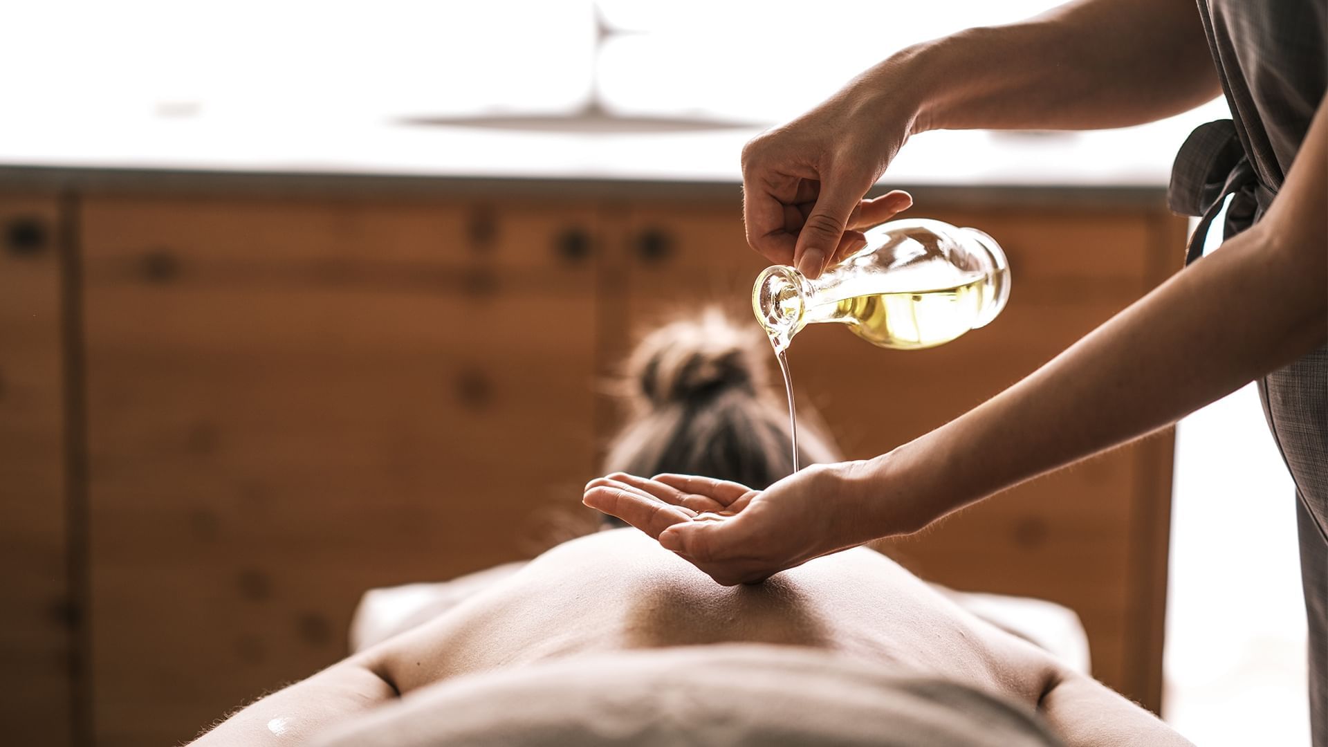 Eine Person gießt Öl auf den Rücken einer Person, die auf einer Massageliege liegt.