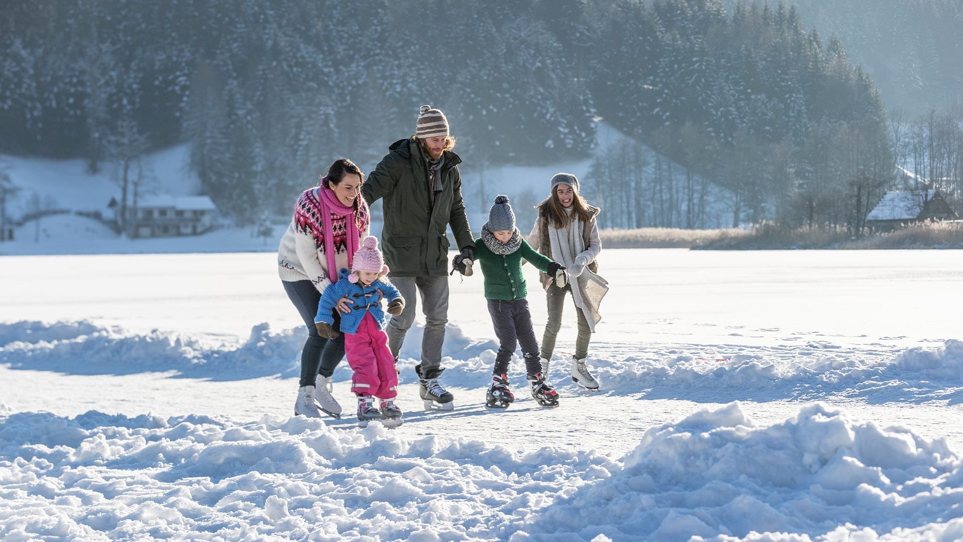 Eine Familie genießt das Winterwetter auf dem Eis, umgeben von Schnee und Bäumen.