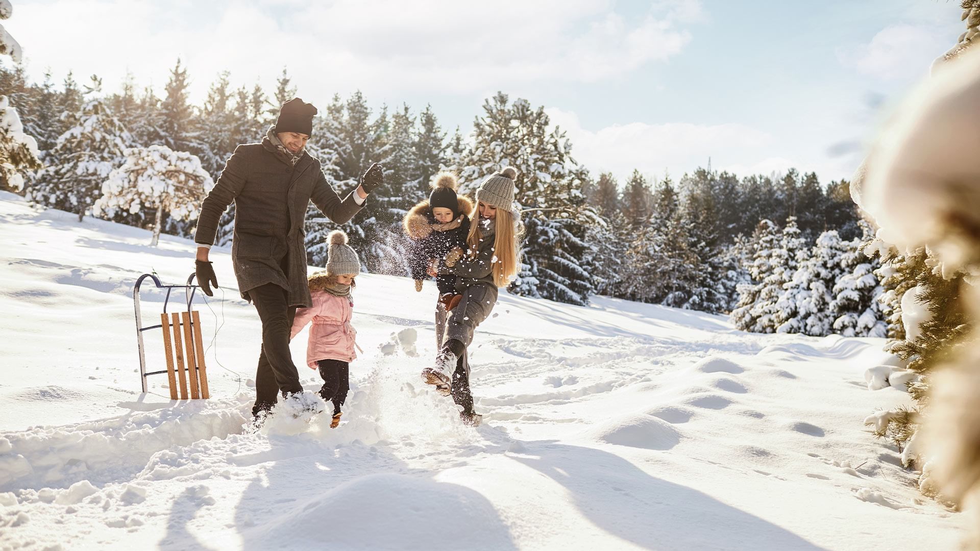 Eine Familie spielt im Schnee mit einem Schlitten, während sie von Bäumen umgeben ist.