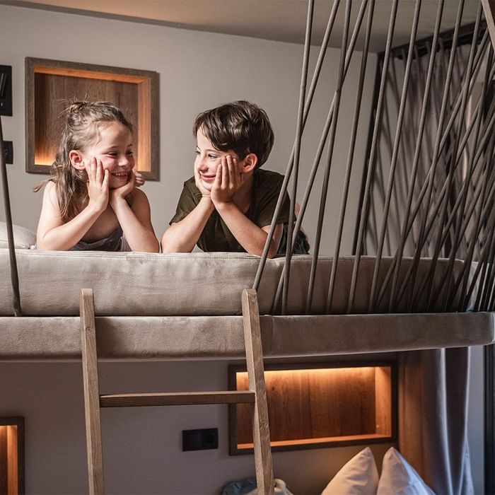 Zwei Kinder auf einem Etagenbett, lachen und sich die Hände vors Gesicht halten.