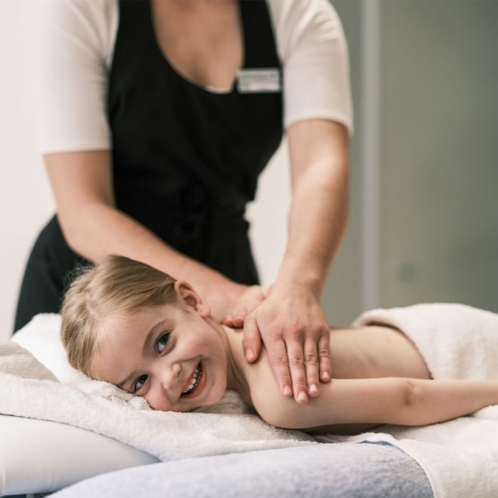 Eine Physiotherapeutin massiert das Kind, das auf einem Tisch mit weißen Handtüchern liegt.