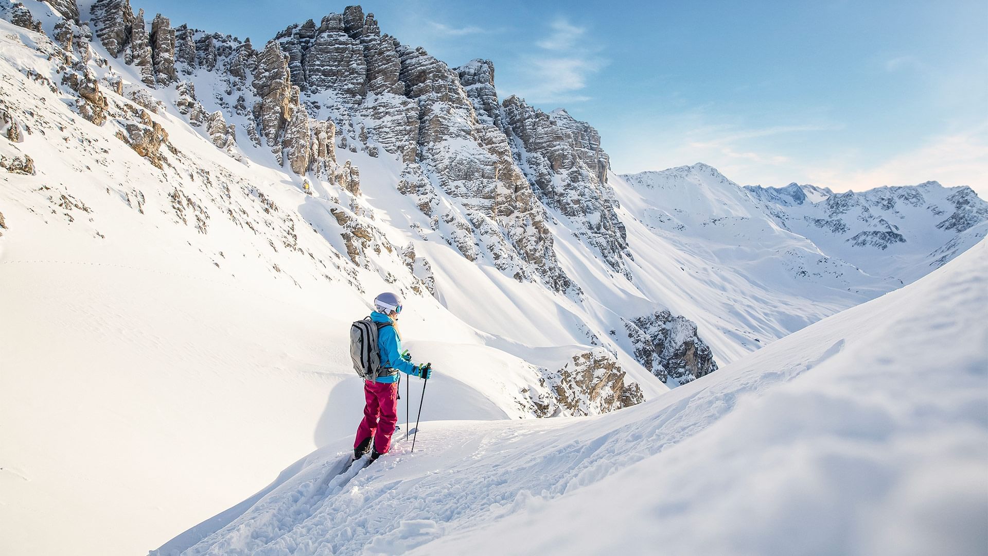 Skifahrerin mit Rucksack und Stöcken auf schneebedecktem Berg in klarer Winterlandschaft.