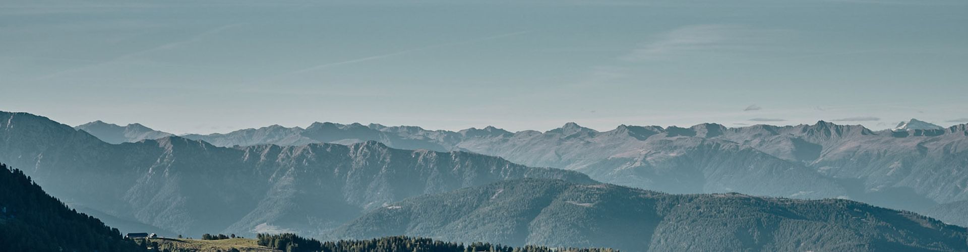 Panorama einer Bergkette mit grünen Wäldern und einem klaren Himmel im Hintergrund.