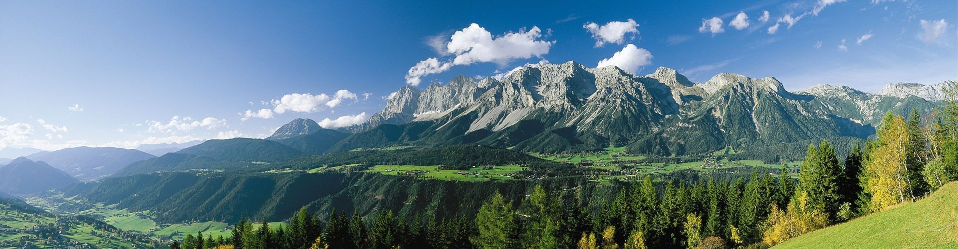 Panorama-Ansicht eines Gebirgszugs mit grünen Tälern, dichtem Wald und einem klaren blauen Himmel.