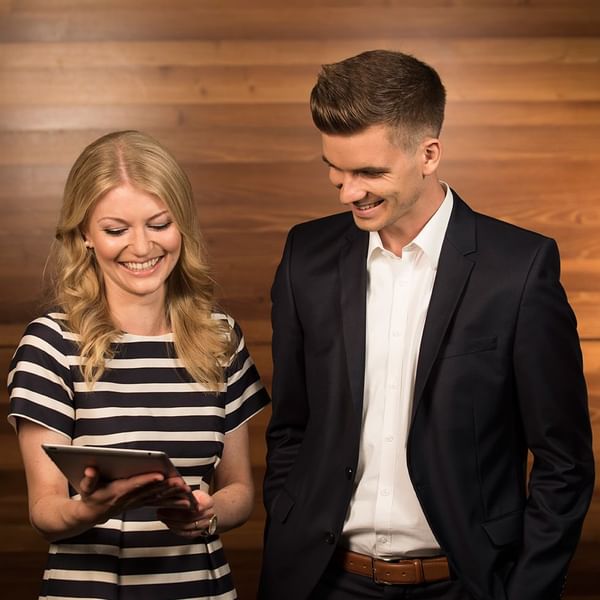 Geschäftsleute betrachten den Bildschirm eines Tablets und lächeln vor einem hölzernen Hintergrund.