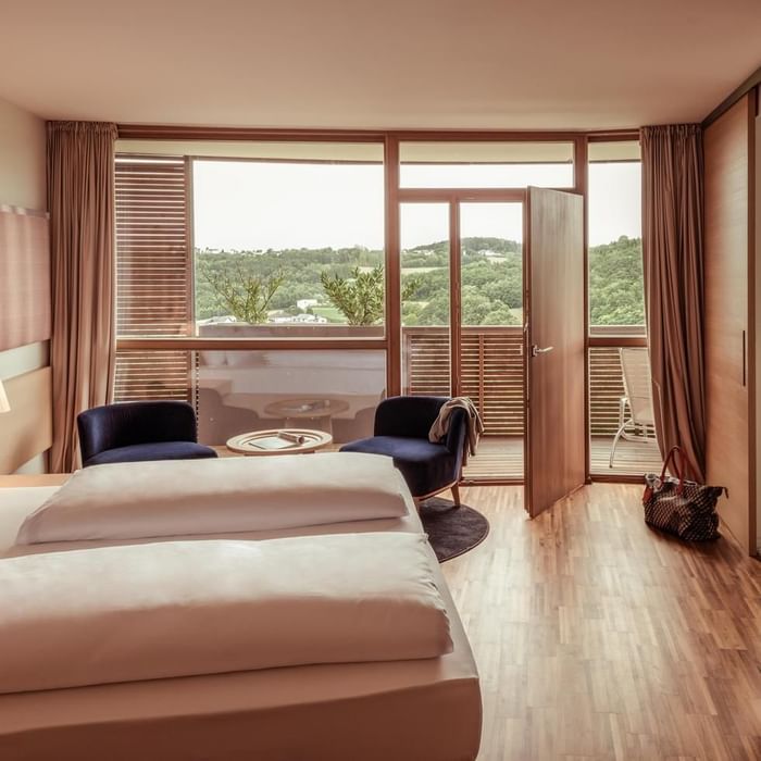 Hotelzimmer mit zwei Betten, Balkon und Aussicht auf bewaldete Hügel.