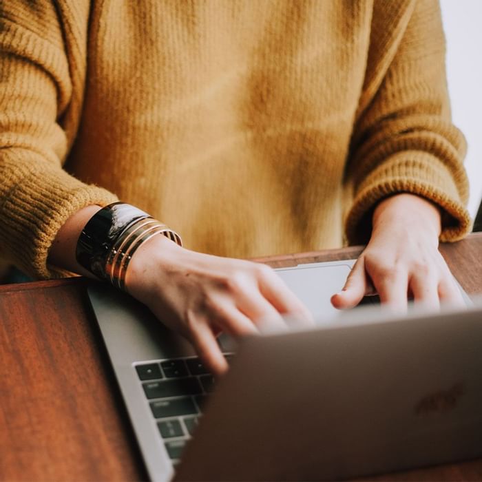 Person in a yellow sweater types on a laptop with one hand, resting the other on the table.