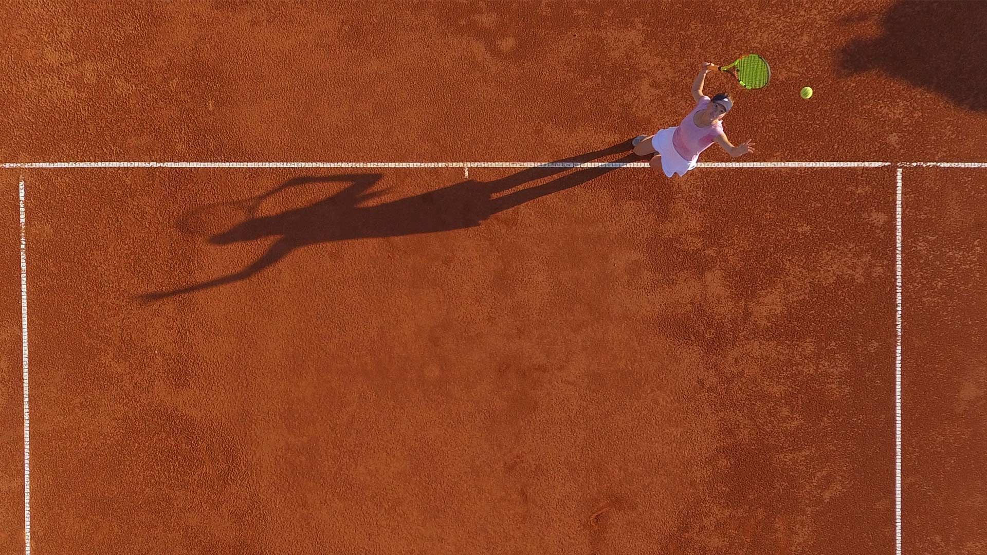Eine Tennisspielerin in Aktion auf einem roten Sandplatz, schlägt den Ball mit ihrem Schläger.