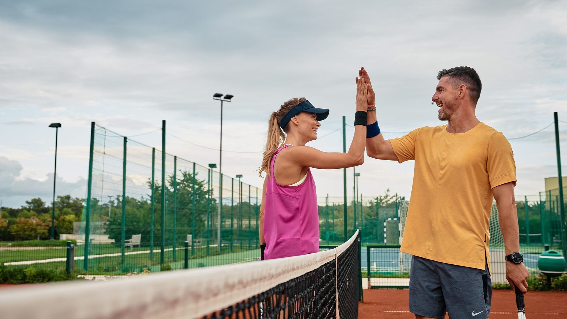 Mann und Frau geben sich auf einem Tennisplatz mit Netz ein High-Five.