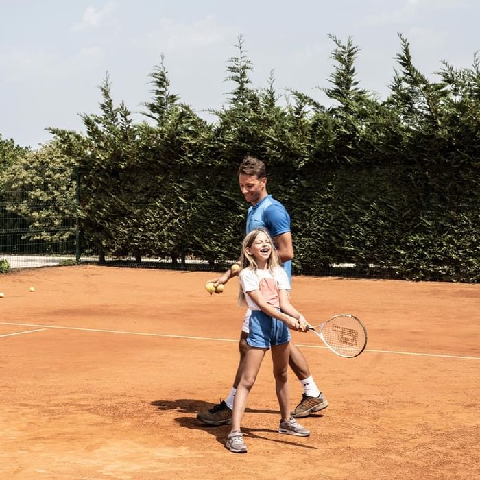 Mann und Mädchen spielen Tennis auf einem Tennisplatz, wobei der Mann dem Mädchen hilft.
