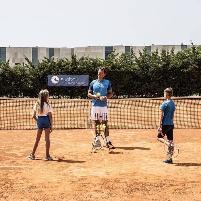 Trainer und zwei Kinder auf einem Tennisplatz, mit einem 