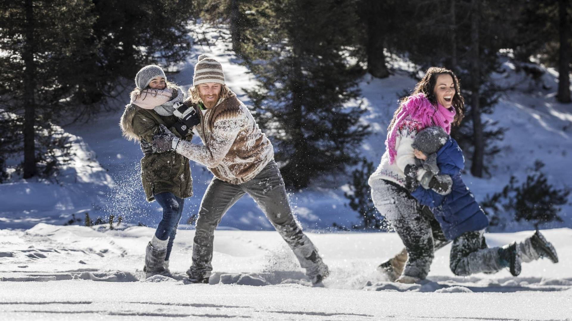 Quattro persone giocano in una battaglia di palle di neve in una zona boschiva innevata.