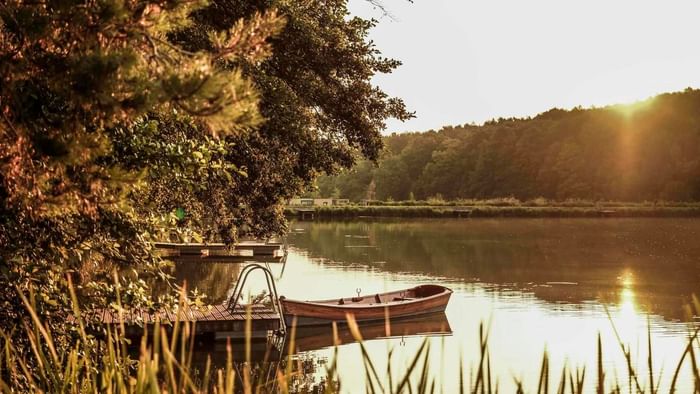Sonnenuntergang über einem See mit Booten, Bäumen und Stegen, umgeben von einem Wald.