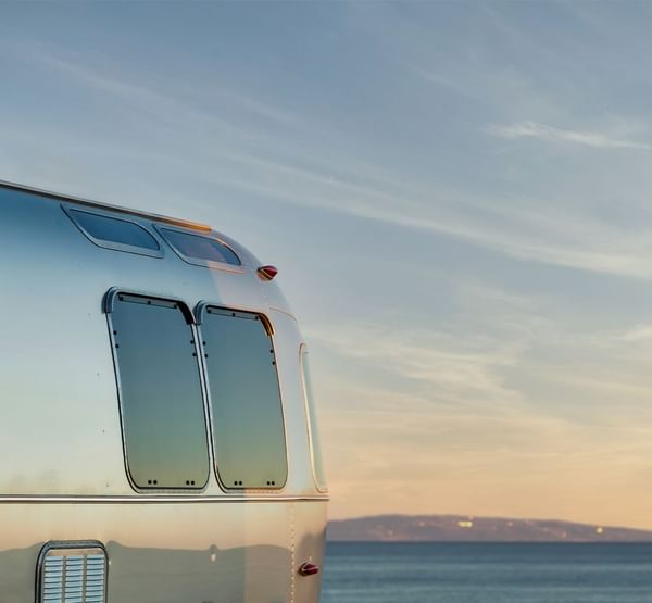 Silberner Wohnwagen am Meer mit Vögeln am Himmel bei Sonnenuntergang.