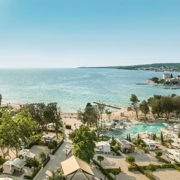 Luftaufnahme eines Campingplatzes am Meer mit Wohnwagen, Bäumen, Pool und Strand.