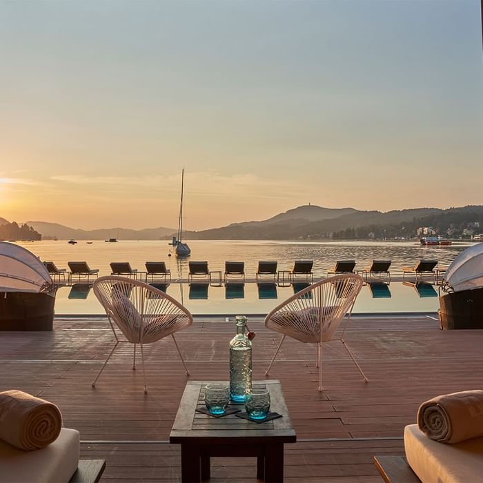 Terrasse mit Lounge-Stühlen, Pool, Booten und Berglandschaft bei Sonnenuntergang.