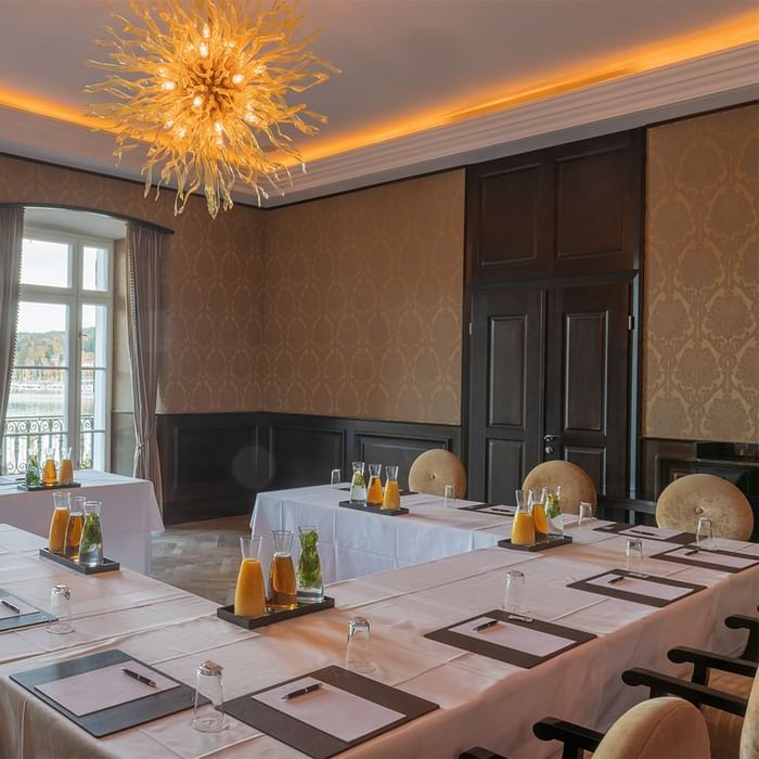 Konferenzraum mit langen Tischen, Getränken, Notizblöcken und eleganter Beleuchtung unter einer auffälligen Deckenleuchte.