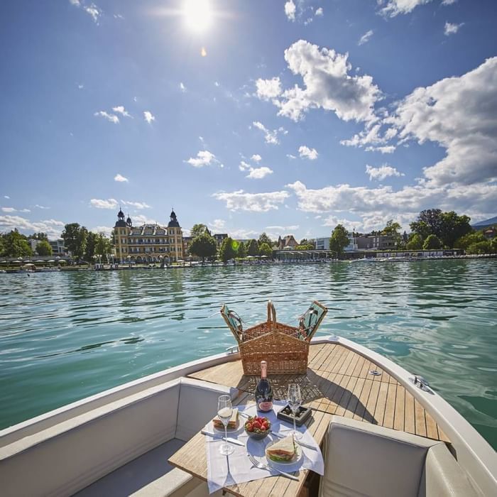 Blick auf den See und Gebäude von einem Boot mit Picknicktisch und Weinflasche.