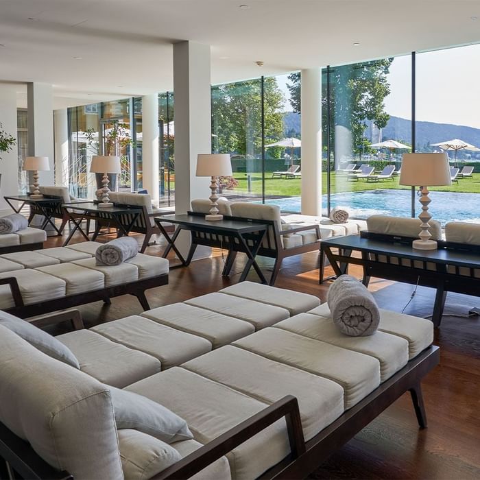 Lounge mit mehreren Sofas und Tischen, großen Fenstern und Blick auf einen Swimmingpool.