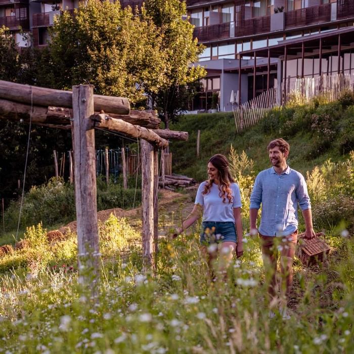 Una coppia sorridente cammina attraverso un prato fiorito, con un edificio residenziale sullo sfondo.