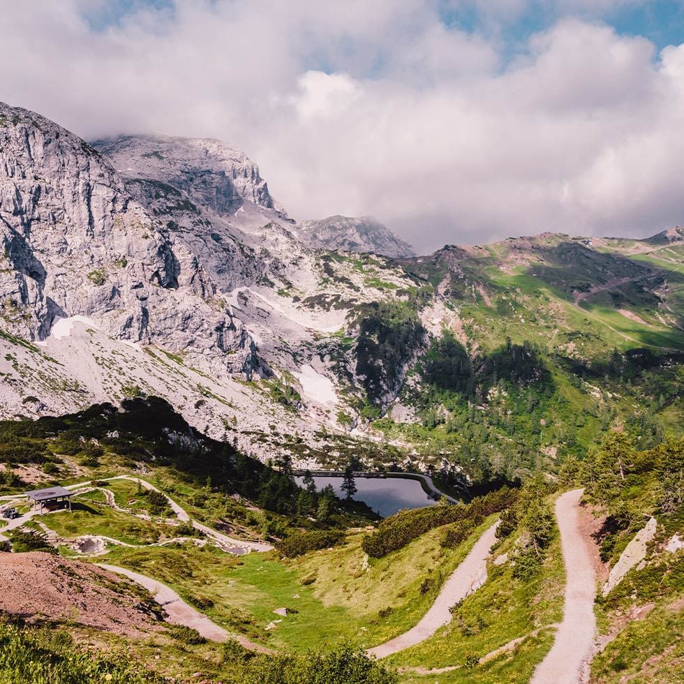 Panorama eines Bergtals mit Wanderwegen, Seen und Wolken am Himmel.