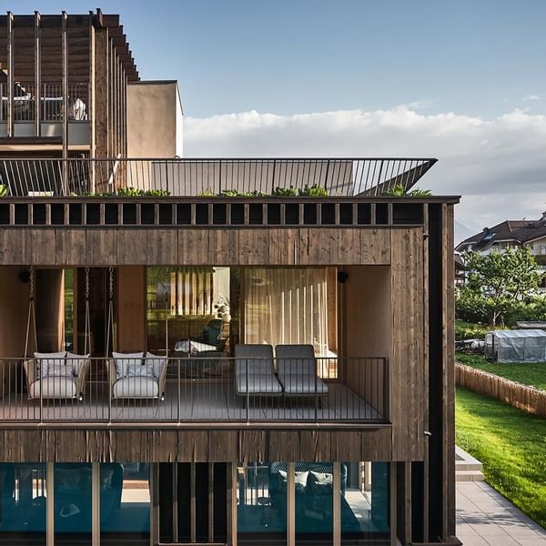 Modernes Gebäude mit Holzfassade, Terrassen, Balkonen und Garten, umgeben von Bäumen und Wiese.
