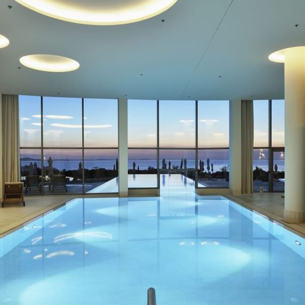 Großer beleuchteter Innenpool mit Panoramablick auf das Meer durch Glaswände und -decke.