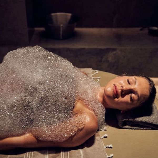 Eine Frau genießt eine entspannende Schaummassage auf einer Liege in einem Wellness-Umfeld.
